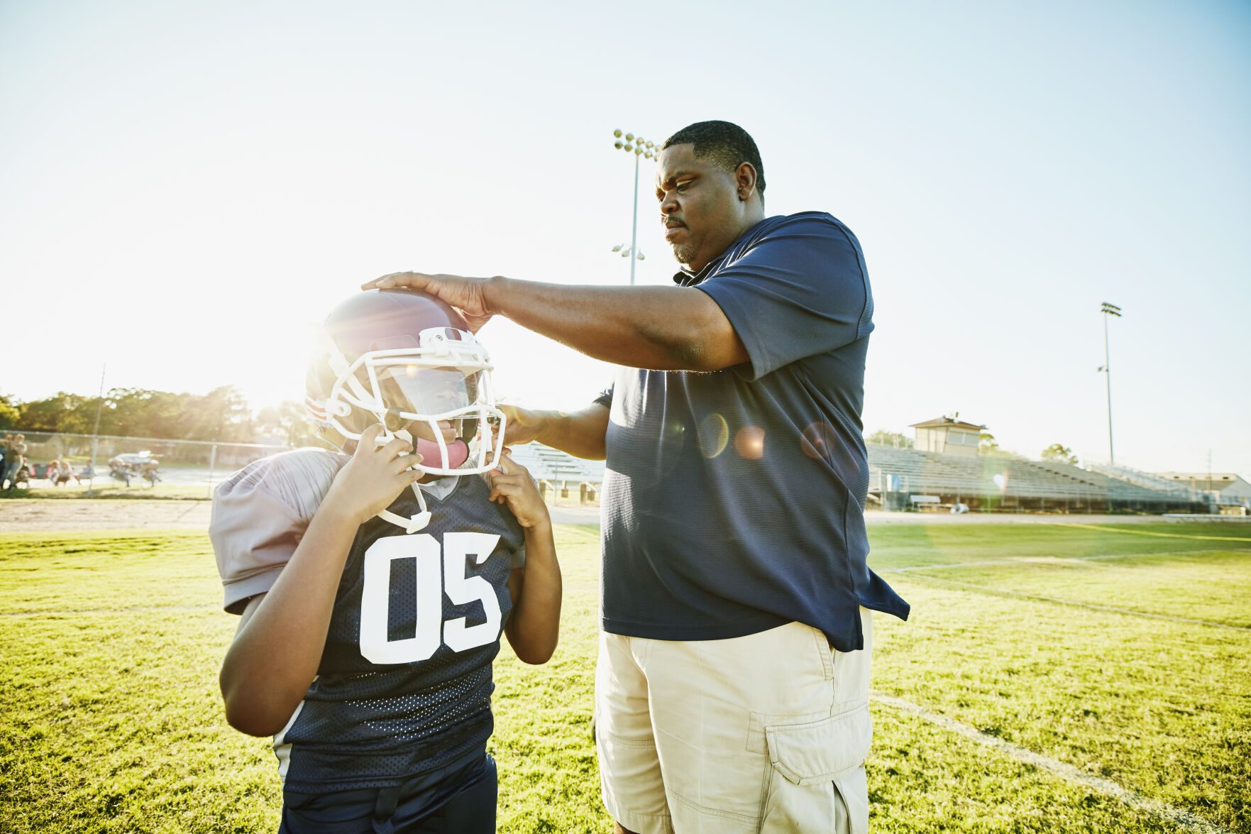Football coach helping young player put on helmet before practice